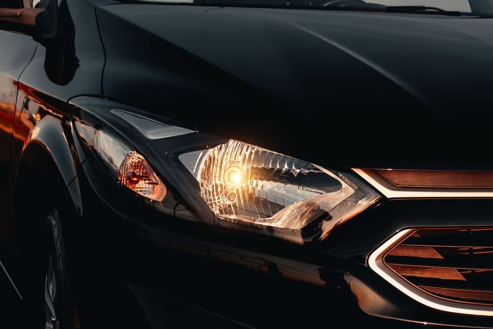 Carro preto com o farol aceso ao entardecer