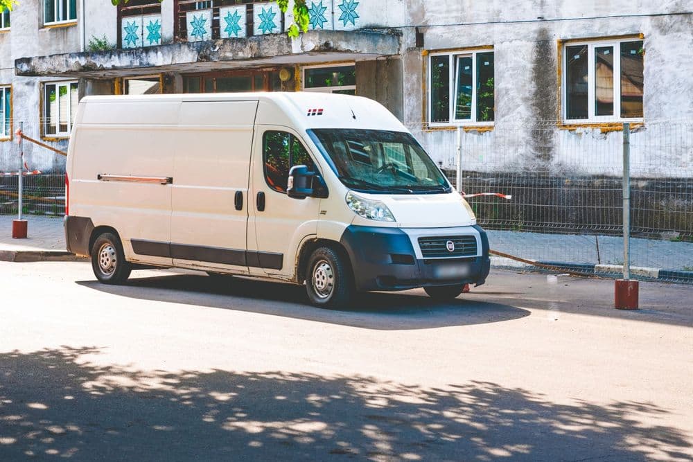 Van branca estacionada numa rua com árvores